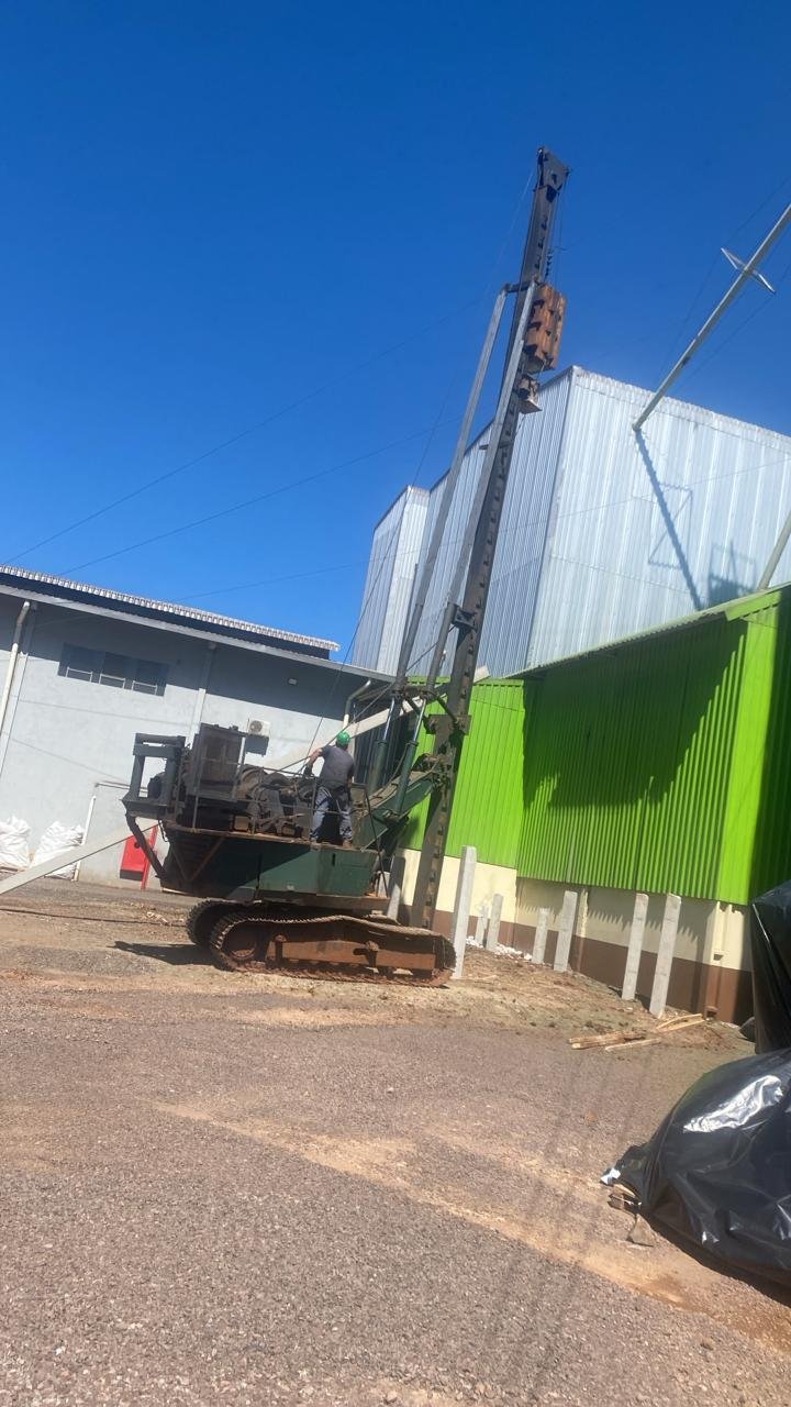 Equipamento bate-estacas sobre esteira operando em área industrial para cravação de perfis metálicos